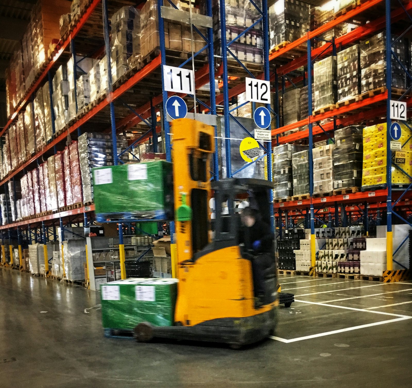Reach truck moving pallets down a high-bay warehouse aisle