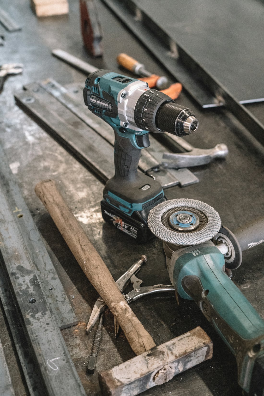 Cordless drill and angle grinder laid out on a steel workbench