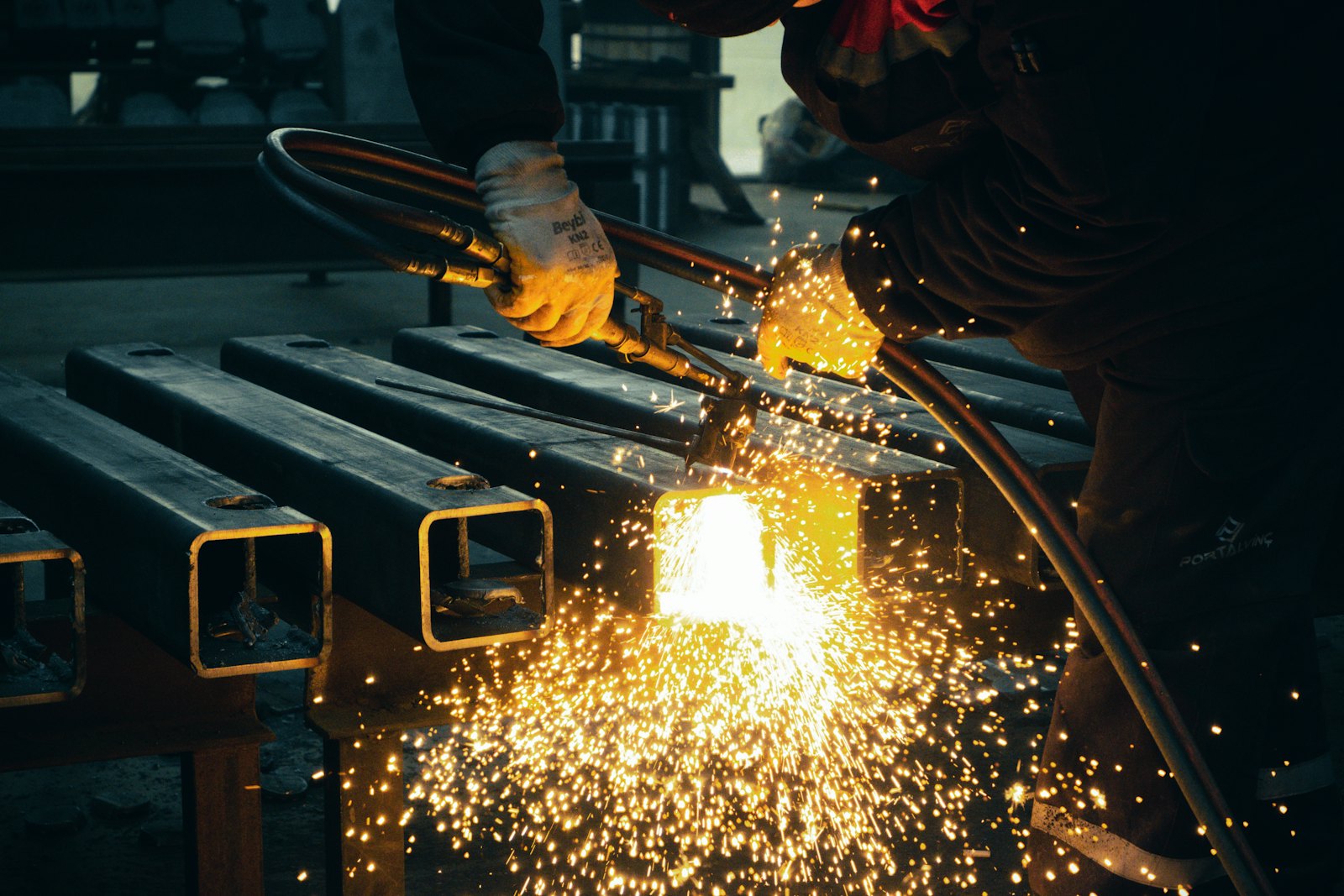 Welder cutting steel box-section, sparks pouring off the cut